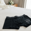 Groom's personalised boxer shorts laid out on a bed on the wedding morning. The black cotton boxer shorts feature custom text, making them a perfect groom gift or detail shot for wedding photography.