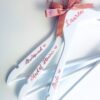 Personalised white bridal party hangers with rose gold hooks and bows, featuring custom names and titles such as Bride, Bridesmaid, and Maid of Honour — elegant customised wedding morning accessories