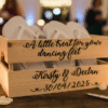 Rustic wooden wedding favor crate filled with white flip-flops for guests' "dancing feet," personalised with "Kirsty & Declan 30/04/2025," an ideal and thoughtful wedding reception detail.
