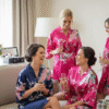 Group of women in matching personalised robes relaxing and celebrating. The woman in a navy bridesmaid robe is holding a champagne glass with the others. Perfect image for a bridal party gift or hen party robes.