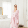 Full length lifestyle image of a woman wearing a light pink kimono style robe with a tie waist, standing in a bright, relaxed setting. This is a simple, elegant option for a bridesmaid robe or loungewear.