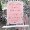 Clear acrylic “Choose a seat not a side” ceremony sign, displayed as modern wedding décor for aisle or entrance.
