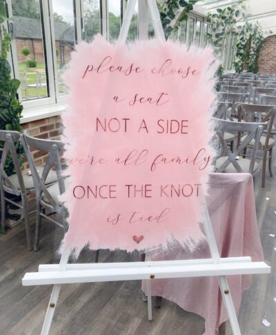 Clear acrylic “Choose a seat not a side” ceremony sign, displayed as modern wedding décor for aisle or entrance.