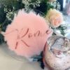 Clear acrylic circle table sign with pink painted background and rose gold lettering, styled with flowers and candles for wedding table décor.