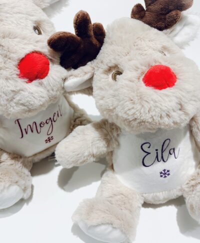 Two personalised soft plush reindeer Christmas toys, sitting side by side on a white background. Each reindeer has a bright red nose, brown antlers, and a white patch on the chest with a custom personalised glitter name (Imogen and Eila) and a snowflake design. Perfect for personalised Christmas gifts and holiday keepsakes.