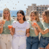 Lifestyle image featuring a close-up of a bride and two bridesmaids at a hen party, all smiling and wearing coordinated short-sleeve t-shirts: the bride in a white tee and the bridesmaids in sage green tees, highlighting personalised hen party t-shirts and group celebrations.